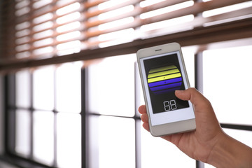 Woman using smart home application on phone to control window blinds indoors, closeup. Space for...