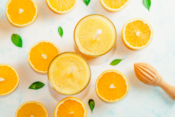 Top view of orange smoothie and orange fruits with green leaves on white background.
