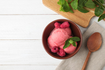 Delicious pink ice cream served with raspberries and mint in bowl on white wooden table, flat lay....