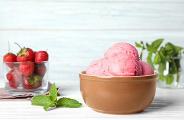 Bowl with delicious strawberry ice cream on white wooden table against light background