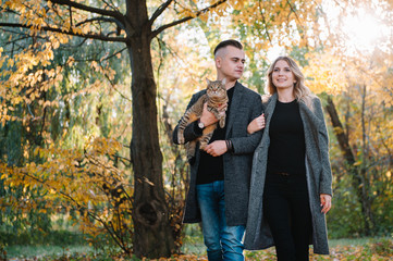 Fototapeta premium Beautiful young couple resting in autumn park. autumn concept. Loving couple resting with their cat.