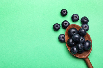 Fresh acai berries with wooden spoon on green background, flat lay. Space for text
