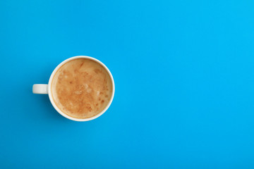 Cup of coffee on blue background, top view. Space for text