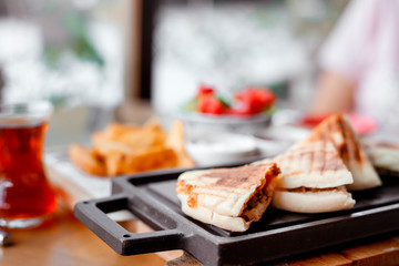 quesadilla sandwich with meat lies on black board on table in outdoor cafe. Turkish tea in glass, potatoes and vegetable salad next to it