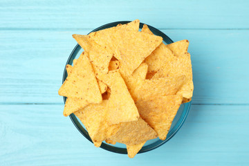 Glass bowl of tasty Mexican nachos chips on light blue wooden background, top view