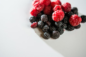 The composition of fragrant and delicious black and red raspberries on a white background are isolated in the studio.