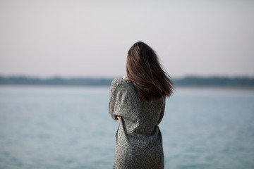 Young very beautiful girl with long hair is standing by the lake. The girl admires the dawn and...