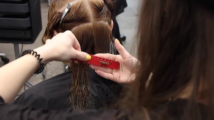 stylist gently combs hair on woman head and cuts with scissors, practices new skills at hairdressing workshop, close-up view