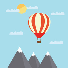 Fototapeta na wymiar A view of a large and hot air balloon flying between clouds in a blue sky above mountain peaks
