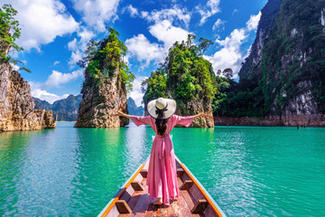 Beautiful girl standing on the boat and looking to mountains in Ratchaprapha Dam at Khao Sok National Park, Surat Thani Province, Thailand. - obrazy, fototapety, plakaty
