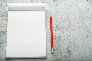 Notepad with red pencil on white plastered wall background, for education, write goals and deeds