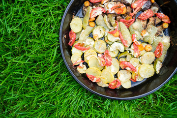 Tasty summer food. Roasted vegetables: zucchini, peppers, carrots, modiors and potatoes. Dish on the background of green grass.