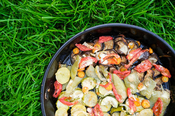 Tasty summer food. Roasted vegetables: zucchini, peppers, carrots, modiors and potatoes. Dish on the background of green grass.