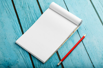Notepad with red pencil on a blue wooden table background, for education, write goals and deeds