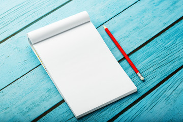 Notepad with red pencil on a blue wooden table background, for education, write goals and deeds