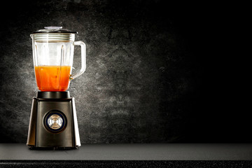 Black blender with juice on a black wall and table background