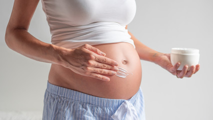 Authentic close up shot of an young pregnant woman in pajamas is applying a moisturizer or sun...