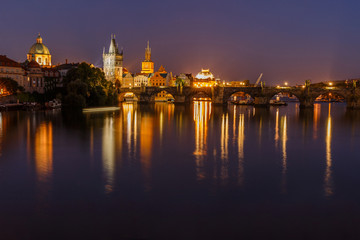 Charles Bridge between districts Old Town and Lesser Town at night in Prague. Old Town tower and historic stone bridge over the Vltava with illumination. Reflection of the colorful lights on the water