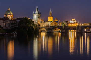 Charles Bridge at night in Prague. Tower and historic stone bridge over the Vltava with illumination between the old town and Lesser Town. Reflections of the colorful lights on the water