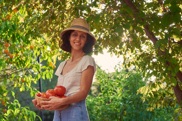  Young woman holds a bowl with natural ecological products from the garden on a sunny sunset, next to a blonde girl watching the vegetables.