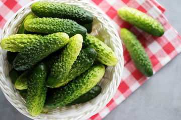 Whole fresh organic cucumbers in a white basket on a gray background. Soft focus. Top view.