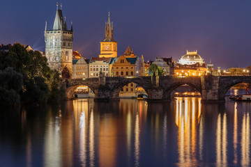 Panoramic view over the river Vltava to Charles Bridge at night in Prague. Old Town tower and historic stone bridge with lighting between the old town and the Lesser Town and reflections on the water.