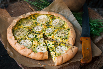 Homemade courgette and goat cheese pie on a dark rustic wooden board background