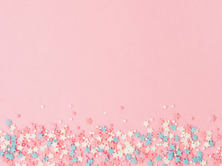 Fototapeta Festive border frame of colorful pastel sprinkles on pink background, copy space top. Sugar sprinkle dots and stars, decoration for cake and bakery. Top view or flat lay obraz