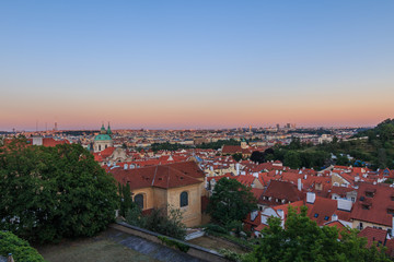 Fototapeta na wymiar View over Prague in the evening. Red evening sun colors the horizon. Cityscape of Prague Castle above the roofs of the Lesser Town and Old Town districts