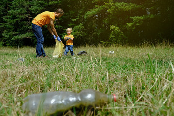 Father and his little son collecting garbage and plastic bottles in the park. Volunteers family...