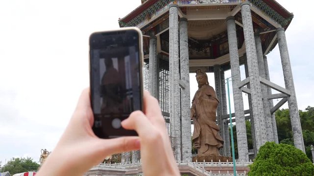 Woman making photos by smartphone of Goddess of Mercy Guanyin or Guan Yin statue in Buddhist Temple. Visiting Spiritual and Cultural Complex. 4k