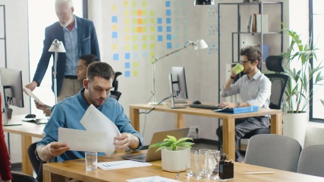 Modern Startup Chief Analyst Works on a Firm Strategy, Looks at Documents Showing Statistics, Graphs and Charts, Corrects them with Pen, Analyzes Data and Information. Diverse Company Office