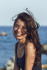 Close-up portrait of cheerful suntanned young woman looking into camera over sea and blue sky...