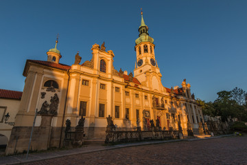 Fototapeta na wymiar Capuchin Church Loreta from Hradcany Square near the Prague Castle. View of the historic Baroque building complex in the Czech capital from the left in the evening sun with blue sky