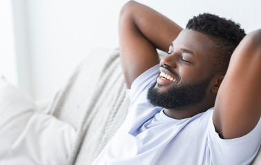 Fototapeta premium Pleased black man relaxing at home on couch