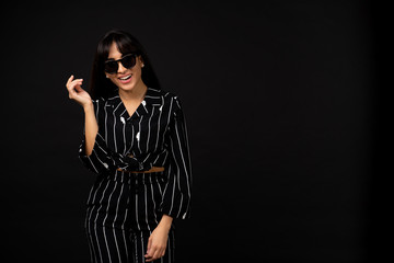Young business girl in a black suit posing for a photo on a black background.