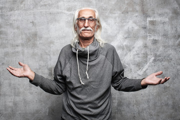 Gray haired Caucasian grandfather with a blank face spreads his arms to the side on a gray background in the studio