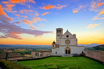 Basilica of San Francis of Assisi at sunset under beautiful glowing orange and blue skies, Italy - obrazy, fototapety, plakaty