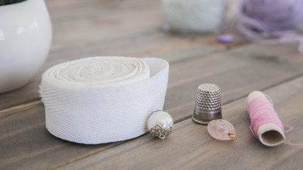 Beads; thimble; white ribbon and pink spool on wooden desk
