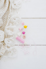 Crochet white fabric; beads and pink spool on wooden desk