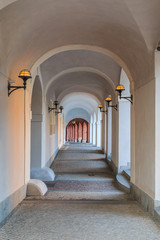 Arched house with in white color with lamps on the walls in Prague on the Hradcany square. Historic windows on the wall. Paving stones in the floor and grandstand on the walls