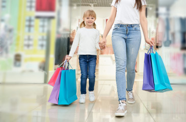 Child and mother with colorful shopping bags in store.