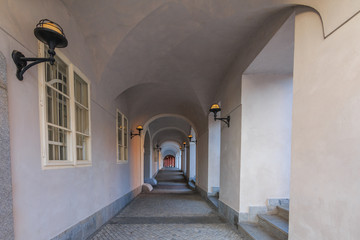Passage in semicircular house with in white color with lamps on the walls in Prague on the Hradcany square. Historic windows on the wall. Paving stones in the floor and grandstand on the walls