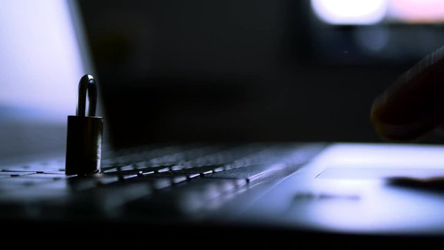 Caucasian hacker operating on laptop computer in a dark room, padlock on focus, conceptual data security footage.