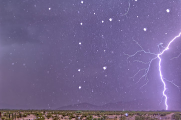 A lightning bolt striking only 1000 feet away in Arizona. The white dots in the image are rain drops frozen in midair by the strobe light effect of the lightning bolt.. 
