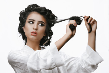 Pretty girl makes styling with hair curlers. Morning preparation. Girl with curlers in bathrobe