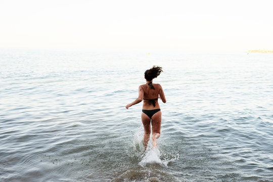 Back view of happy brunette running into the sea.