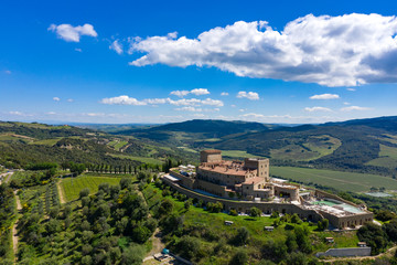 Fototapeta premium A castle stands on top of a Tuscan hill surrounded by cypress trees. Mountains shape the background landscape. 