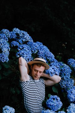 Young man wearing hat standing among hydrangeas