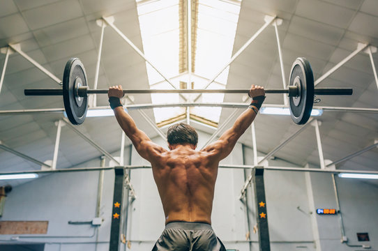 Rear view of man lifting barbell in gym